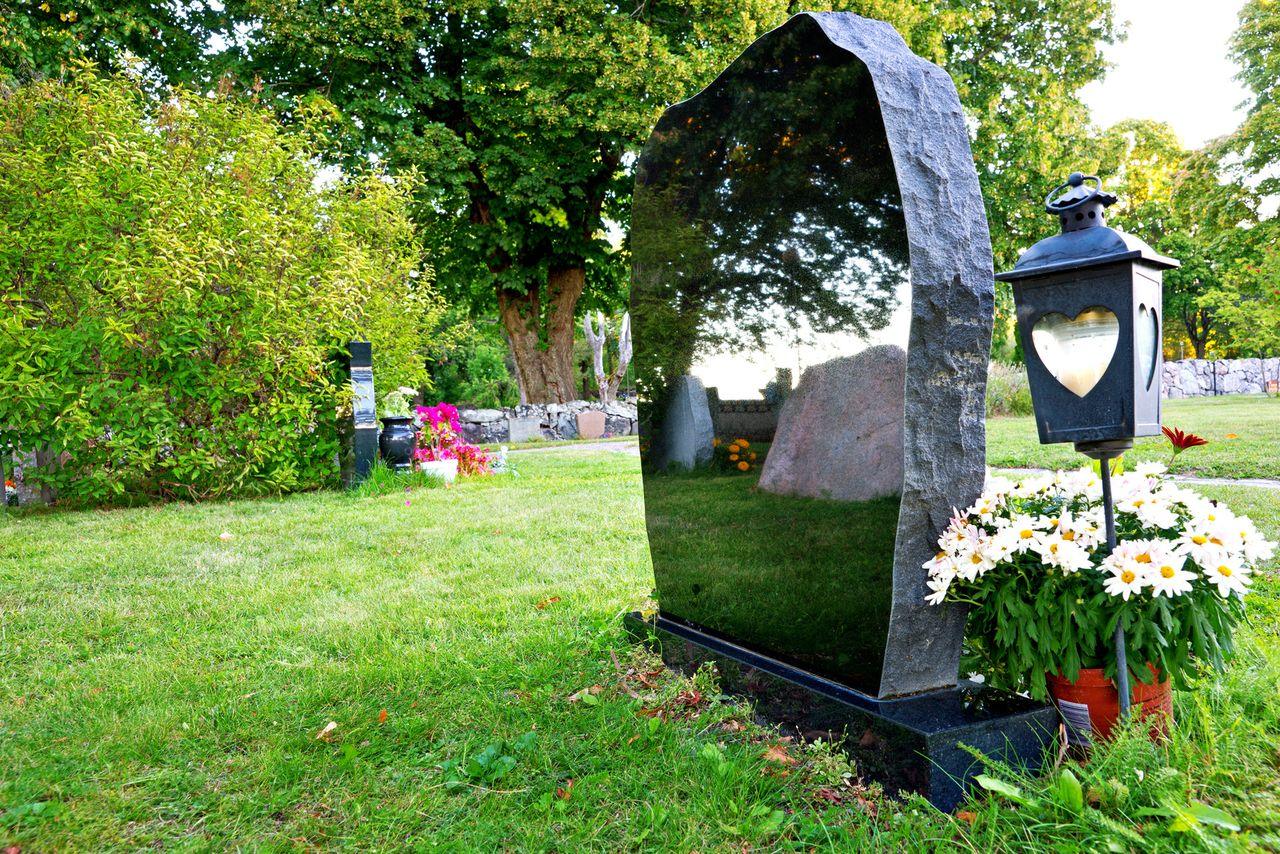 Polished black granite gravestone with lantern and flowers in a cemetery